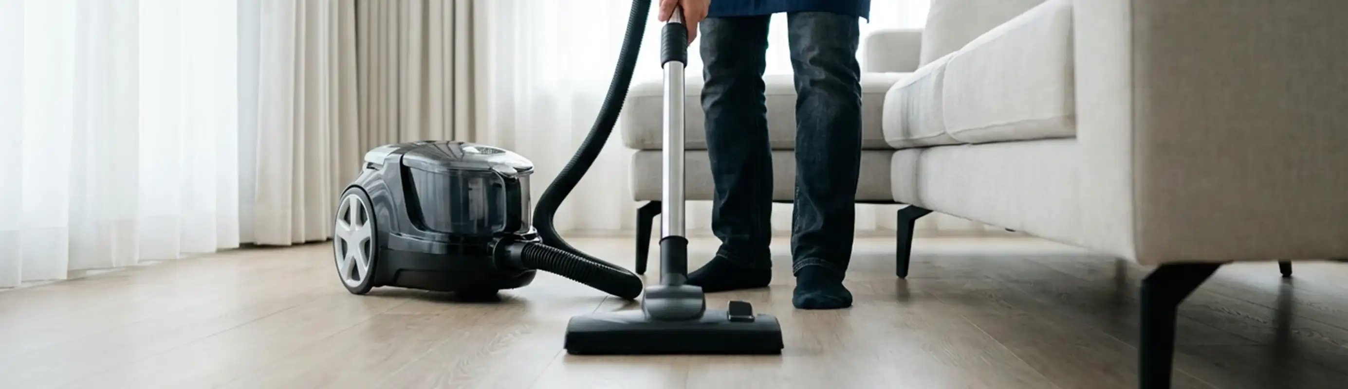 Professional house cleaner vacuuming a living room floor with a canister vacuum cleaner, Albuquerque, NM.