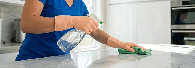 Maid service worker spraying and wiping a kitchen countertop with a microfiber cloth for sanitizing, Albuquerque, NM.
