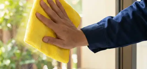 House cleaner wiping a glass window with a yellow microfiber cloth for streak-free cleaning, Albuquerque, NM.